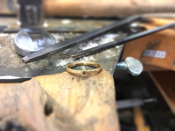 Handgefertigter Verlobungsring mit Stein, fotografiert vor Goldschmiedewerkzeugen